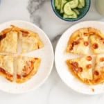 Naan pizza on two white plates with cucumbers on side.