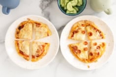 Naan pizza on two white plates with cucumbers on side.