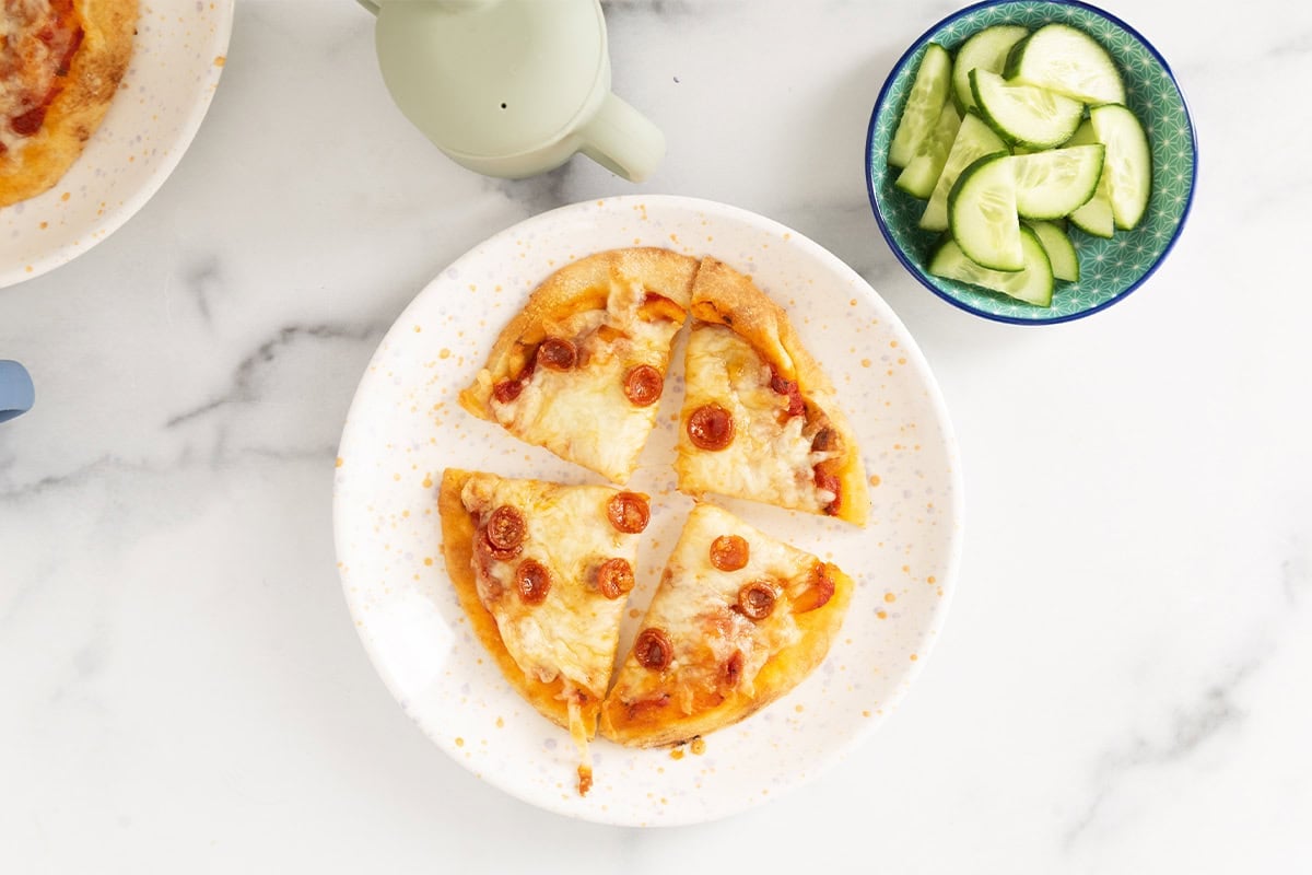 Naan pizza on white plate with cucumbers on side.