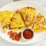 Omelet pizza cut into slices on white plate with dipping sauce.