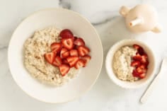 Two white bowls with overnight steel cut oats and strawberries.