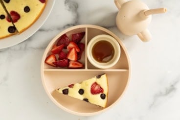 Pancake cake slice on kids plate with strawberries and syrup.