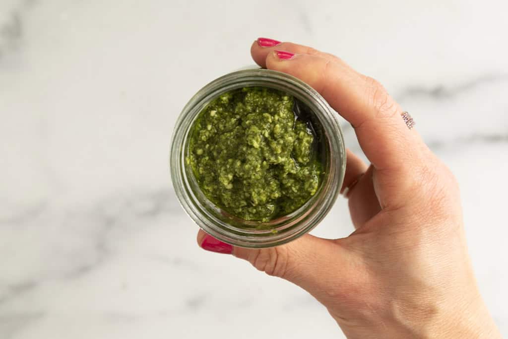 Hands holding small glass jar of pesto.