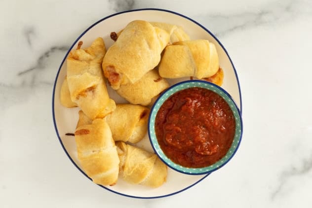 Pizza crescent rolls on white plate with dipping sauce.
