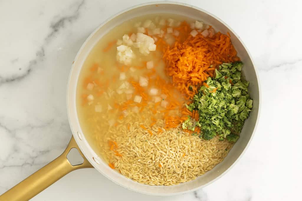 Veggies with orzo and broth in a pan for veggie orzo.