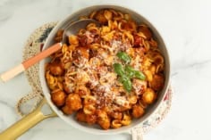 Chicken meatball pasta in pan with cheese and basil on top.