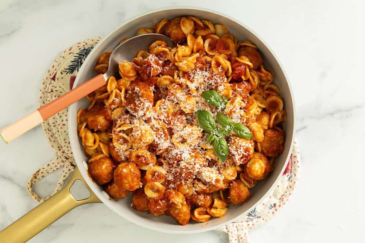 Chicken meatball pasta in pan with cheese and basil on top.