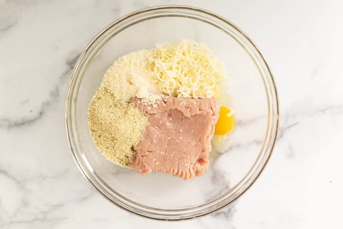 Ingredients for chicken parmesan meatballs in glass bowl.