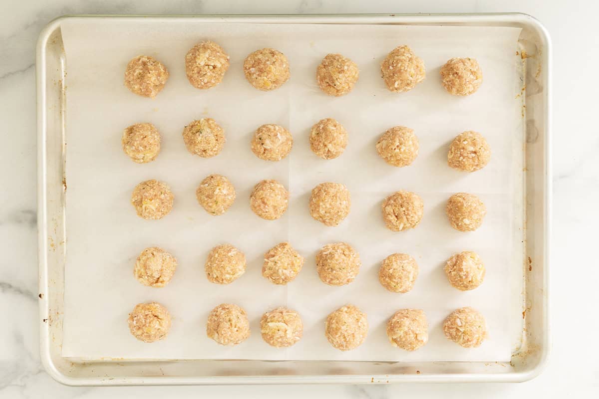 Chicken parmesan meatballs on baking sheet before baking.
