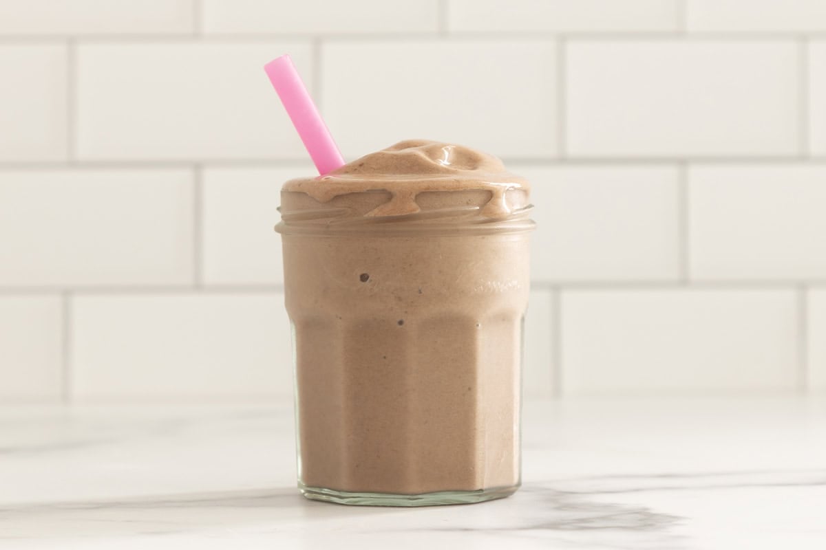 Chocolate peanut butter banana smoothie in glass cup with straw.
