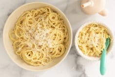 Parmesan noodles in two bowls with blue spoon and cup.