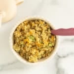 White bowl of veggie quinoa with spoon on countertop.