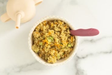 White bowl of veggie quinoa with spoon on countertop.