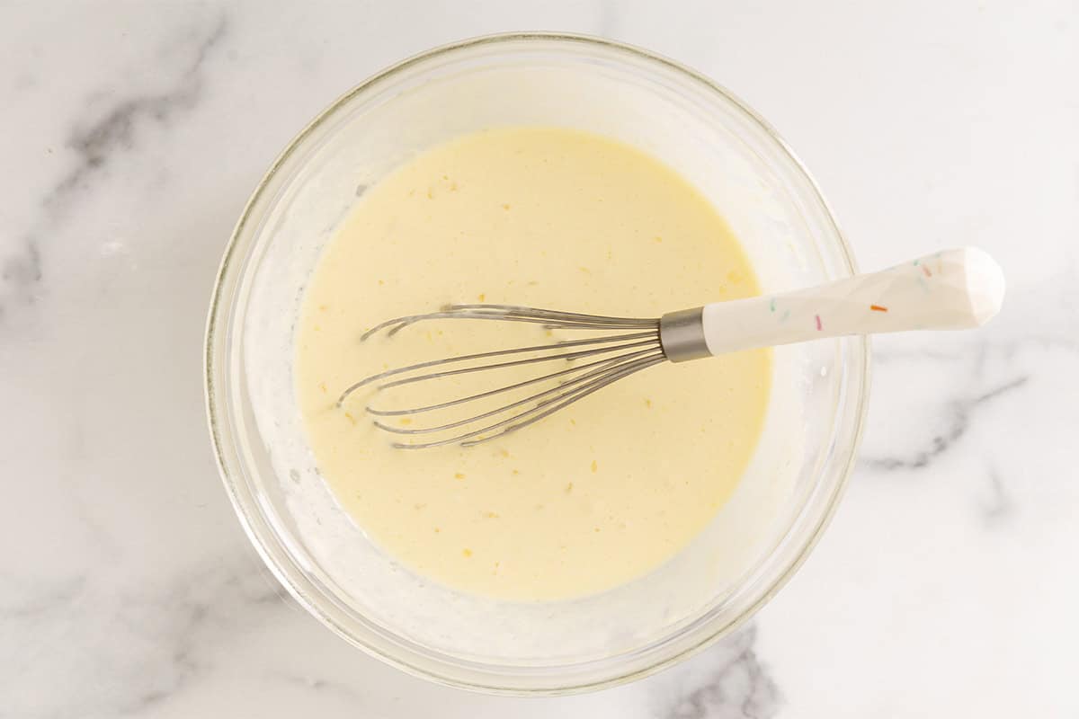 Liquid ingredients for waffle sticks in glass bowl with whisk.