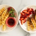 Waffle sticks on two plates with strawberries.