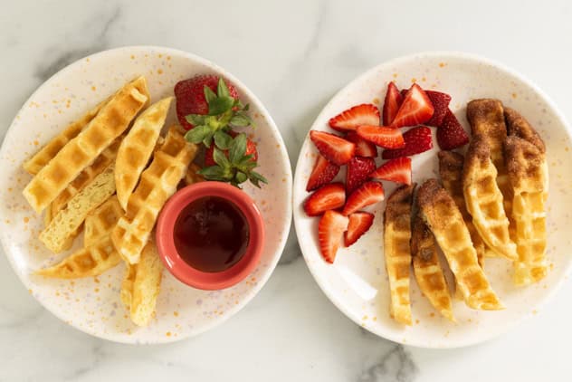 Waffle sticks on two plates with strawberries.