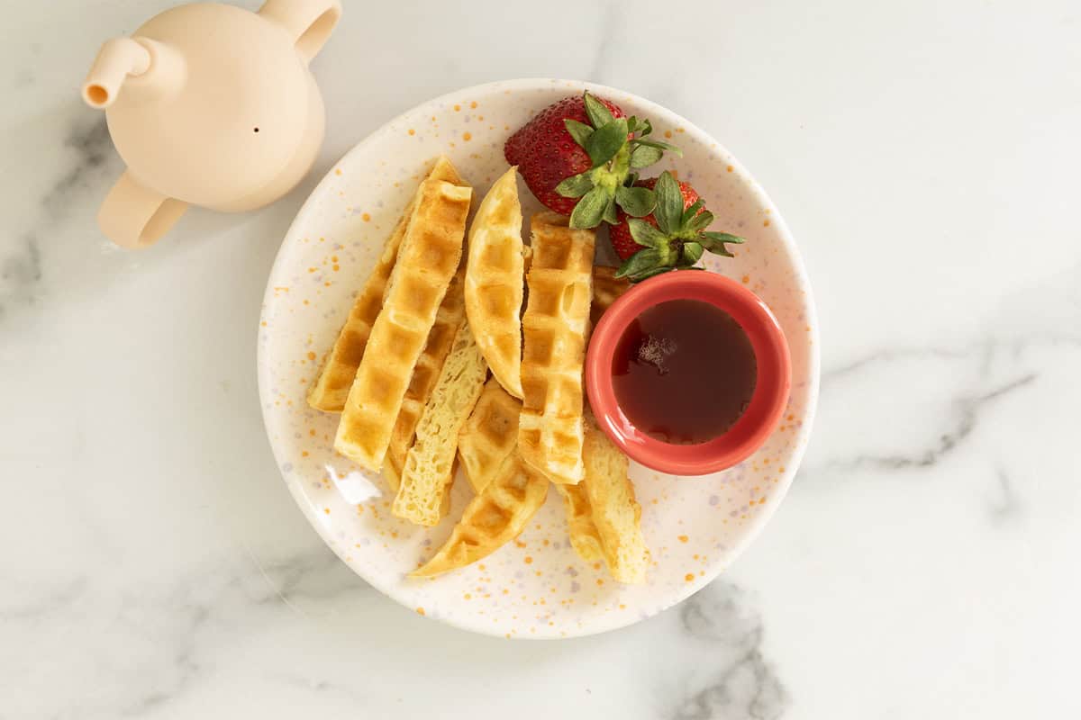 Waffle sticks on plate with strawberries and syrup.