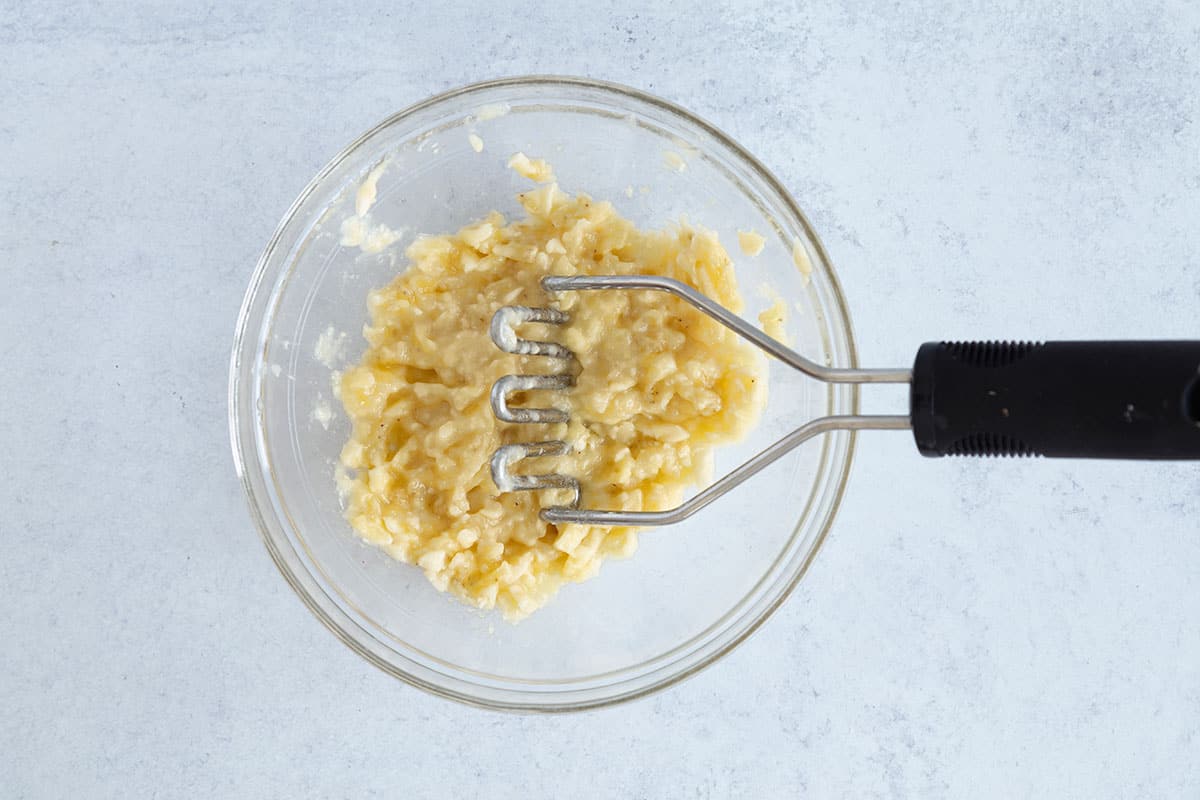 Banana being mashed in glass bowl for breakfast cookies.