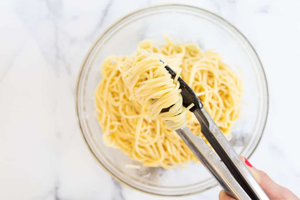 Making parmesan noodles in glass bowl with thongs.