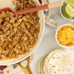 Making ground chicken tacos with tortillas and toppings in multiple bowls.