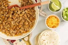 Making ground chicken tacos with tortillas and toppings in multiple bowls.
