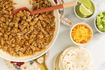 Making ground chicken tacos with tortillas and toppings in multiple bowls.