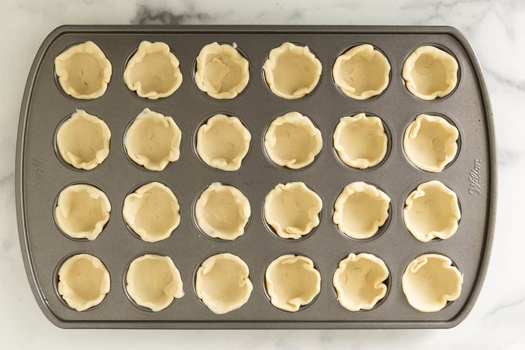 Putting pie dough in mini muffin pan.