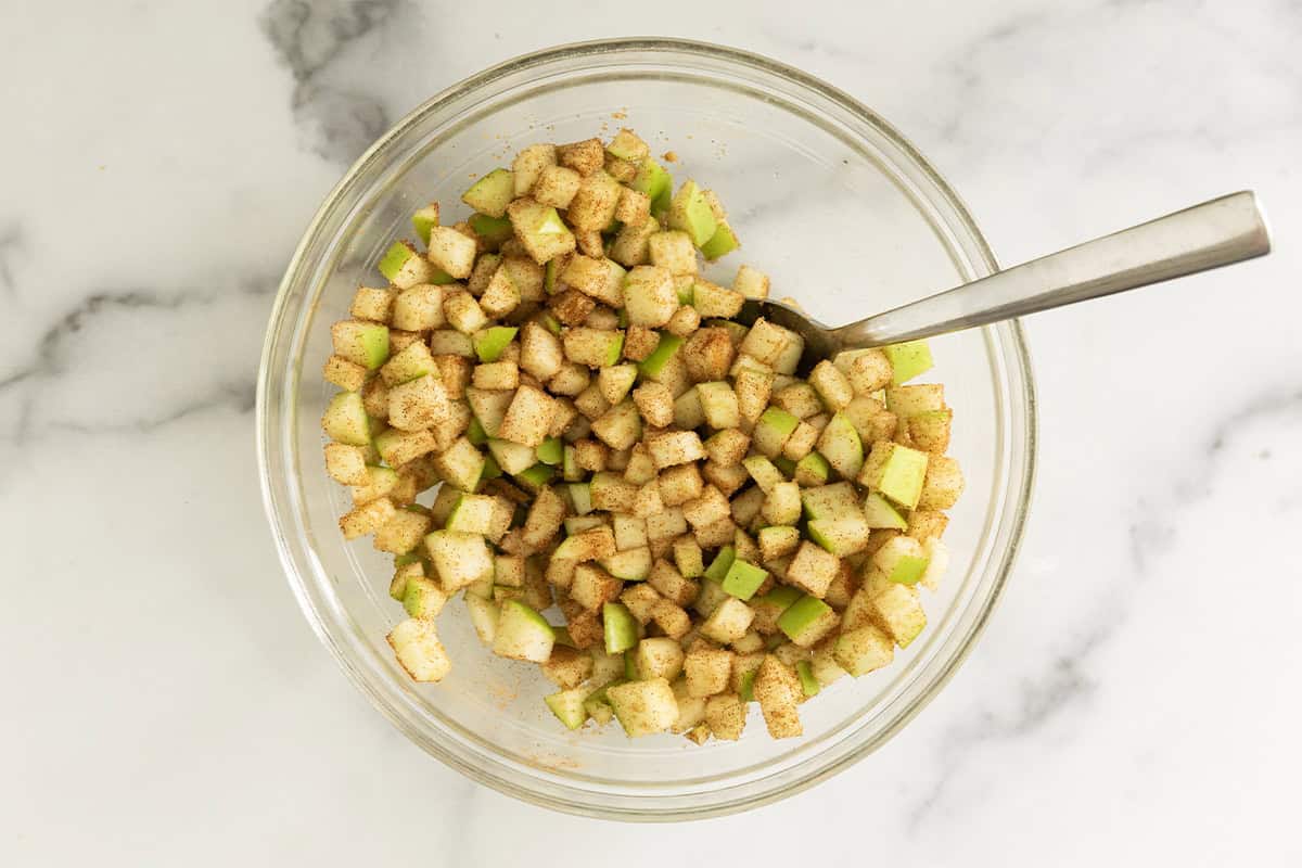 Making apple pie filling in glass bowl with spoon.