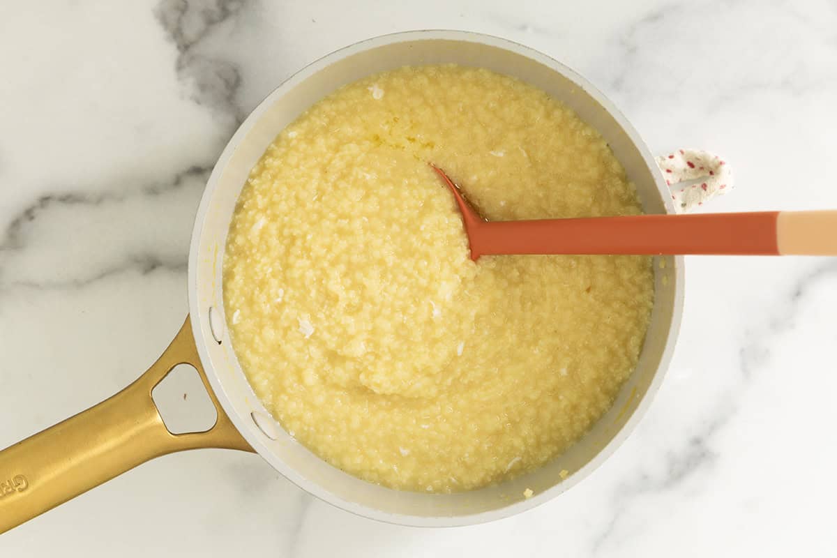 Spatula stirring pastina with egg in pot.