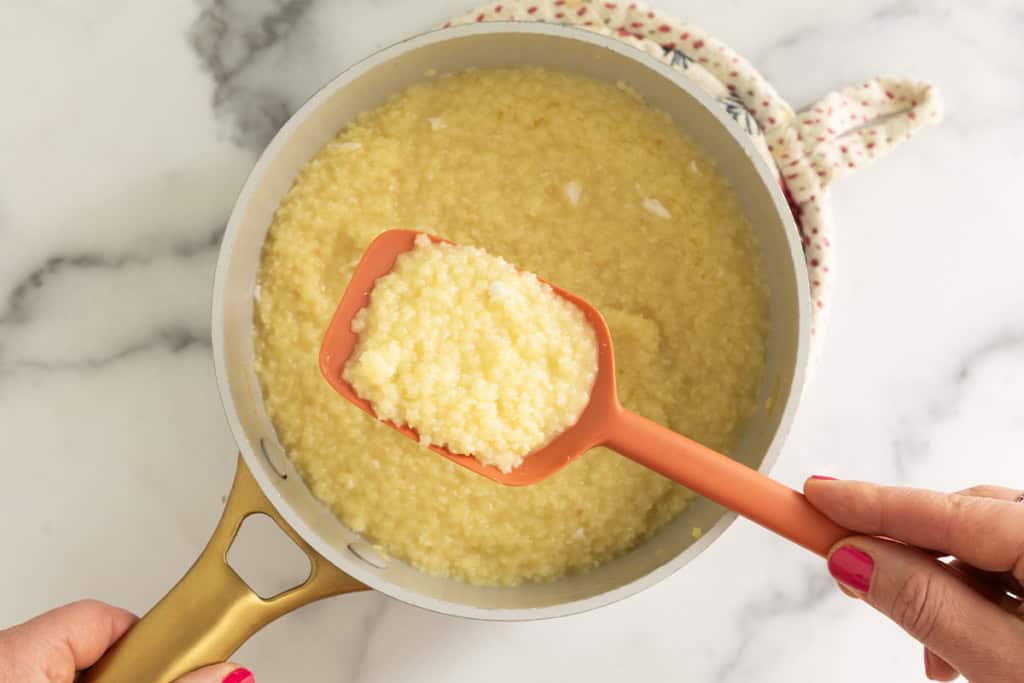 Spatula stirring pastina with egg in pot.