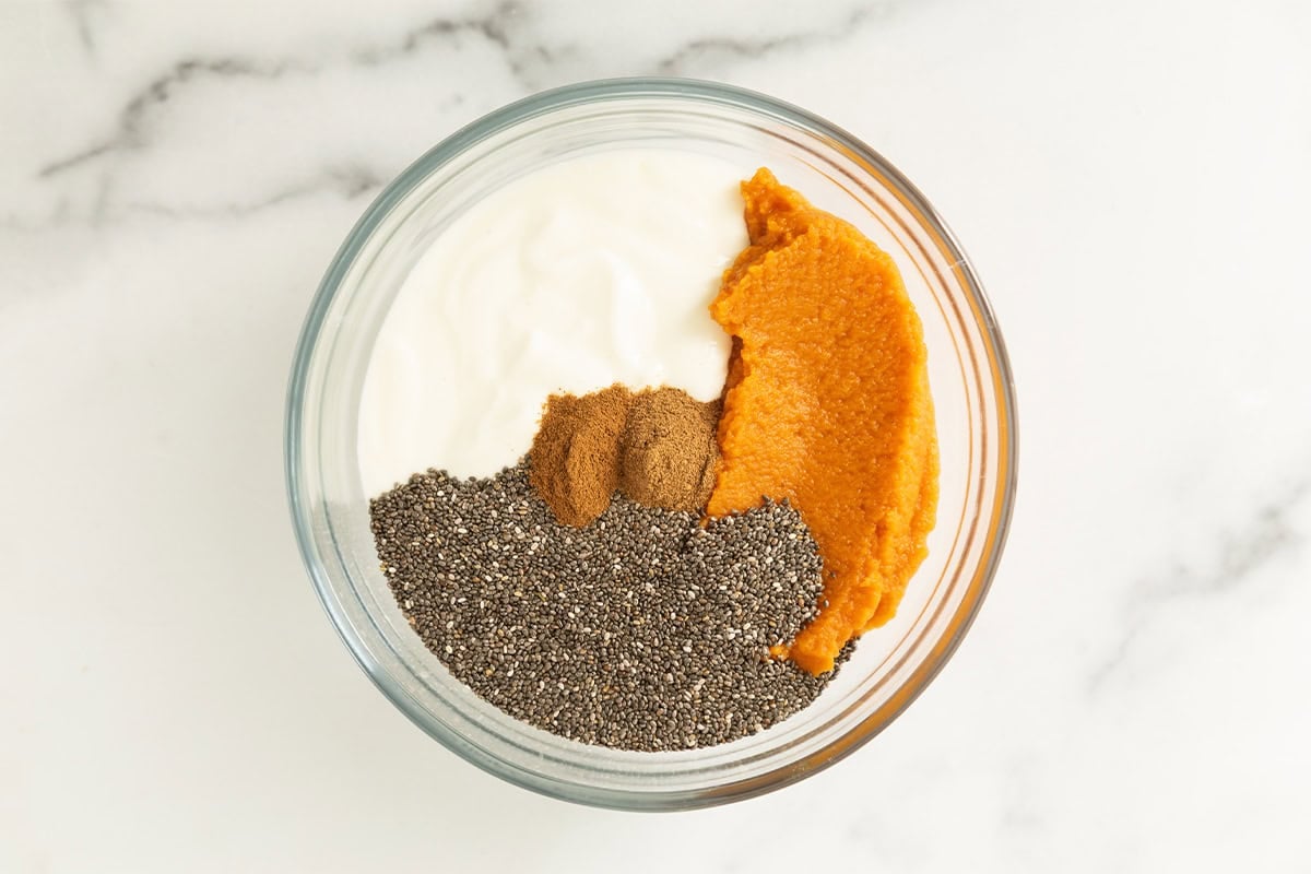 Ingredients for pumpkin chia seed pudding in glass bowl.