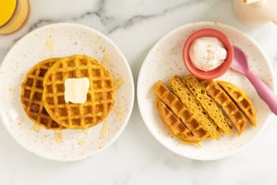 Pumpkin waffles on two plates with butter.