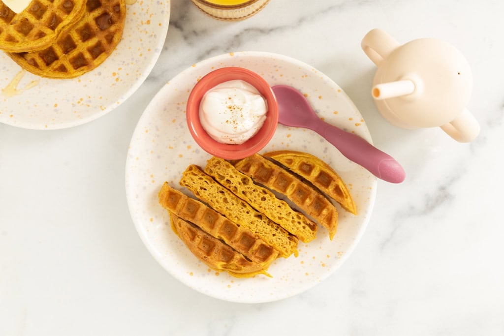 Pumpkin waffle cut on kids plate with cup and fork.
