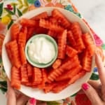 Hands holding plate of watermelon fries with dip in middle.