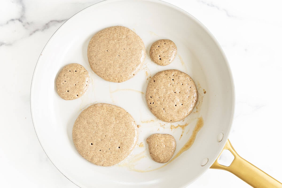 Buckwheat pancakes cooking in a skillet before flipping.