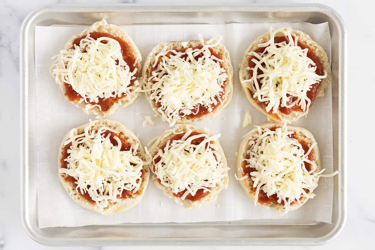 English muffins topped with mozzarella cheese on a baking sheet.
