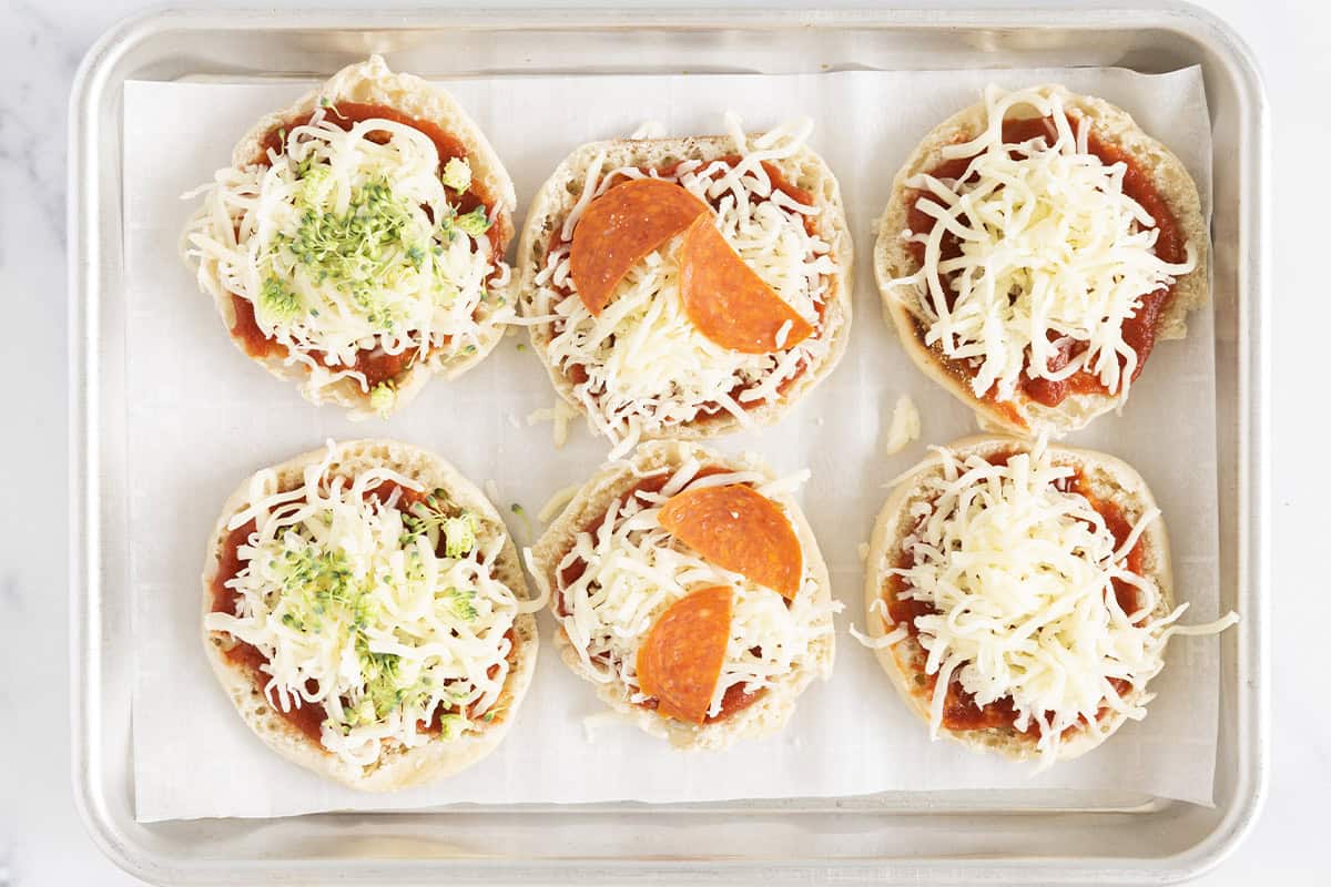English muffins topped with cheese and pizza toppings on a baking sheet.