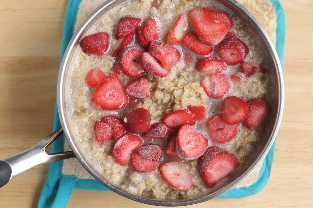 Oatmeal cooking with frozen strawberries in a pot.