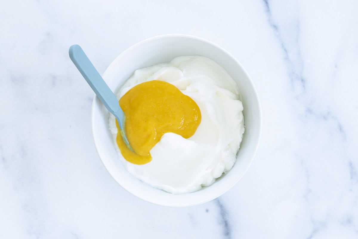 Mango puree added to yogurt in a bowl.