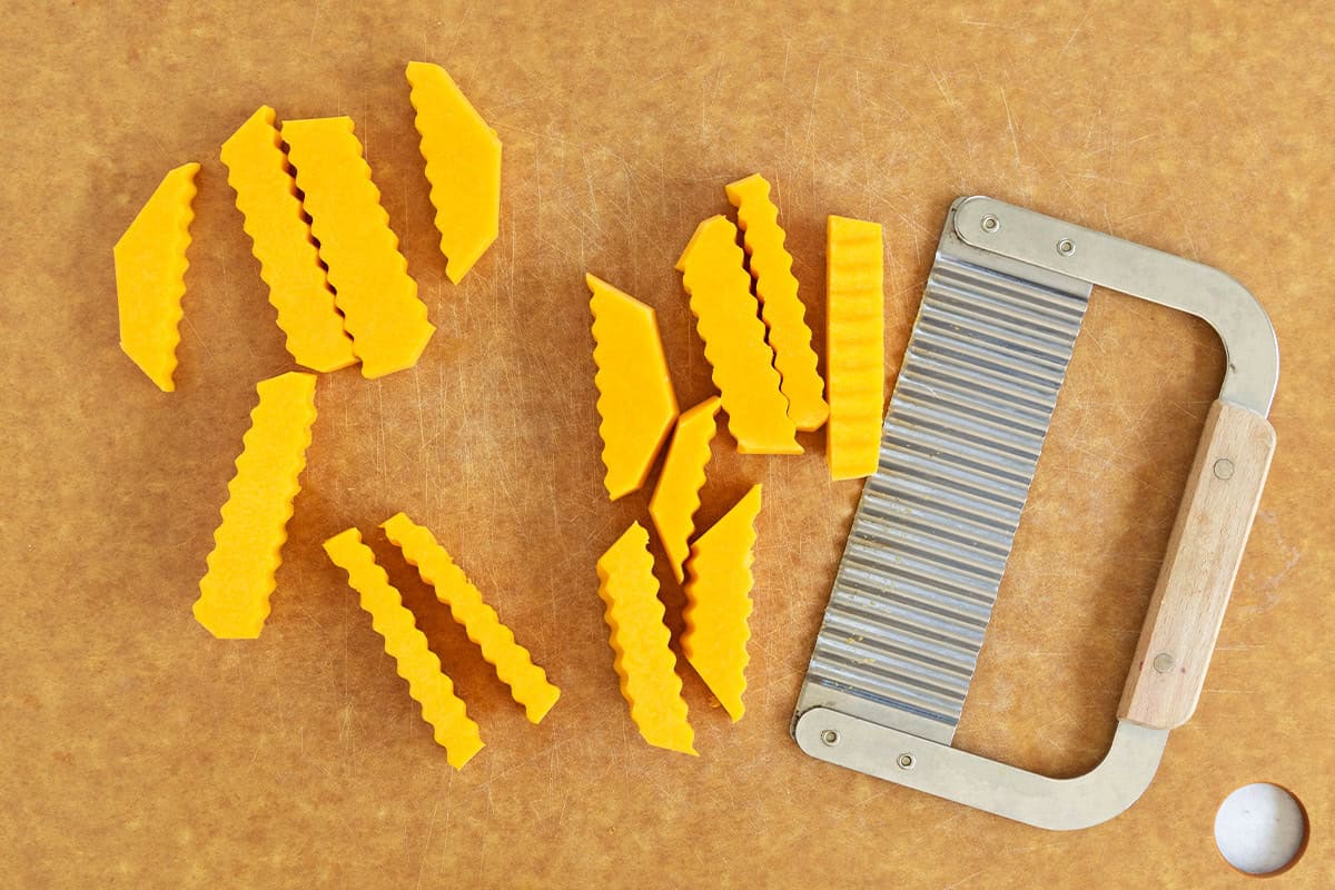 Butternut squash cut into fries and shapes on a cutting board.
