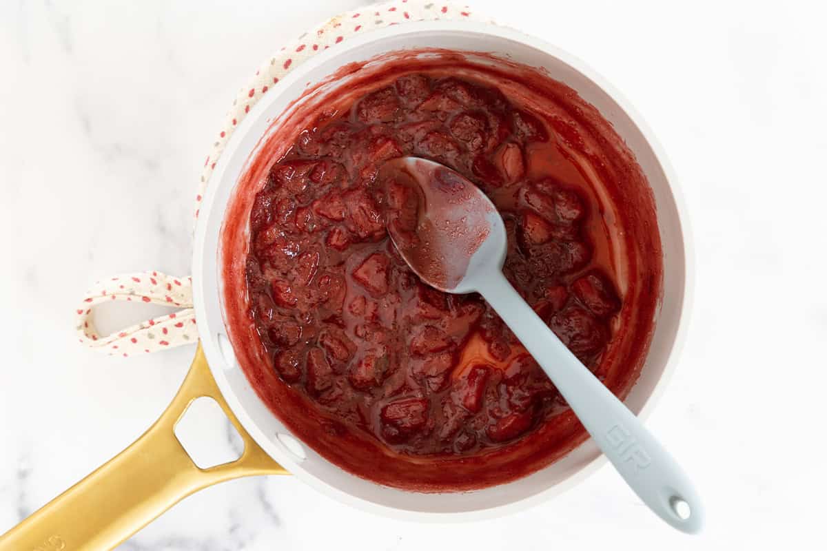 Cooked strawberry sauce in a saucepan with a spoon.