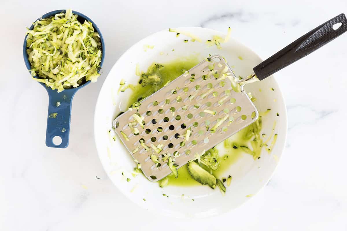 Grated zucchini beside a box grater.