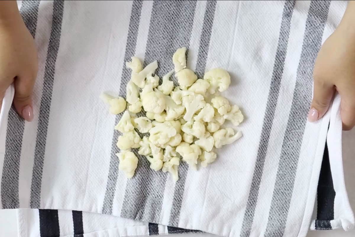 Drained cauliflower resting on a striped kitchen towel.