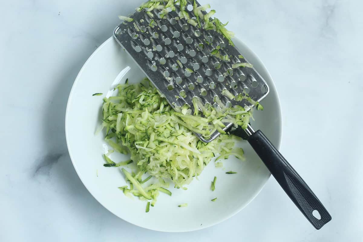 Shredded zucchini on a plate with a box grater.
