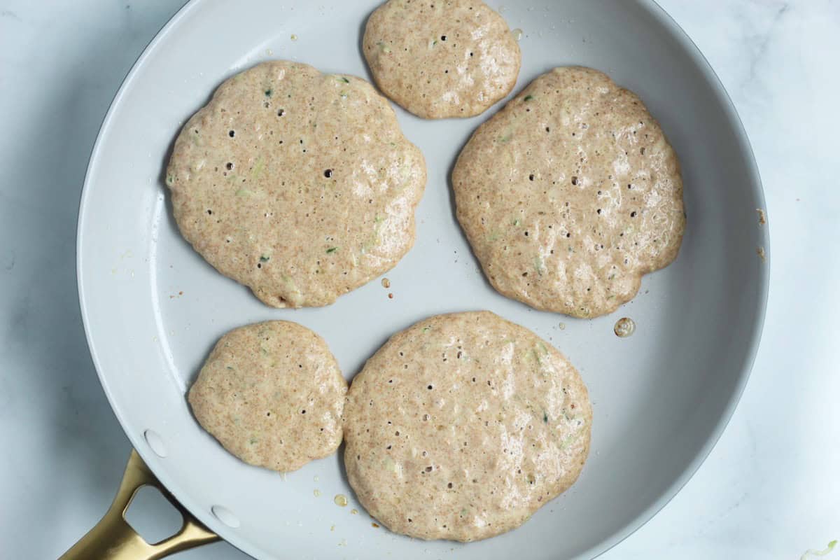 Zucchini pancakes cooking in a skillet.