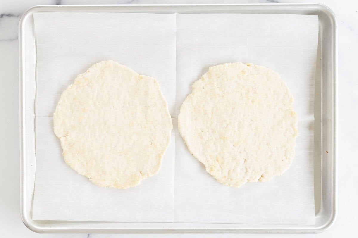 Two pizza dough rounds on a parchment-lined baking sheet.