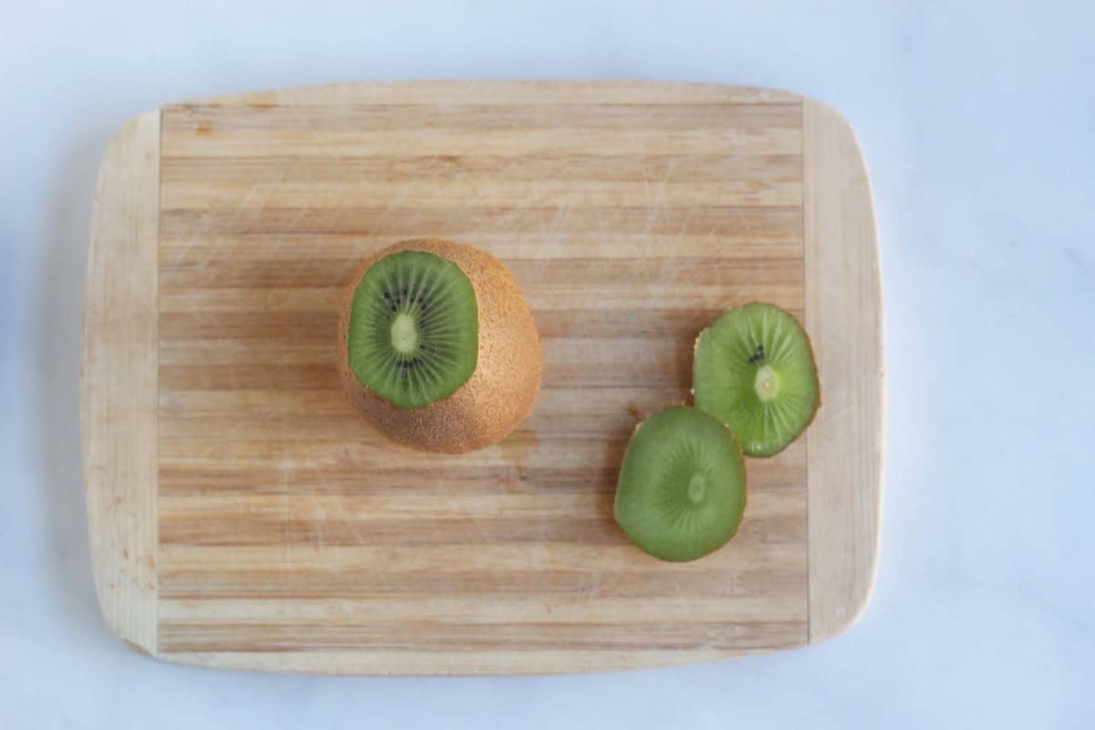 Kiwi with its ends trimmed on a cutting board.