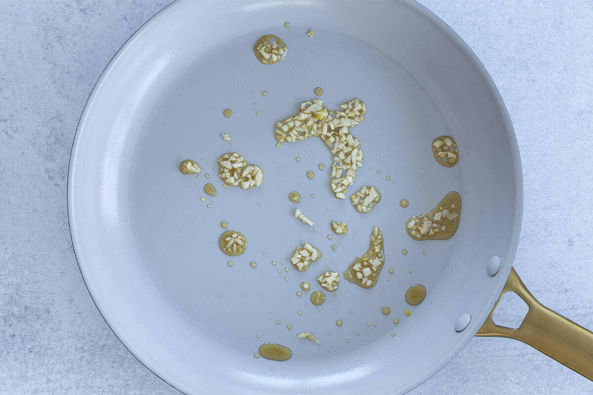 Garlic cooking in sesame oil in a skillet.