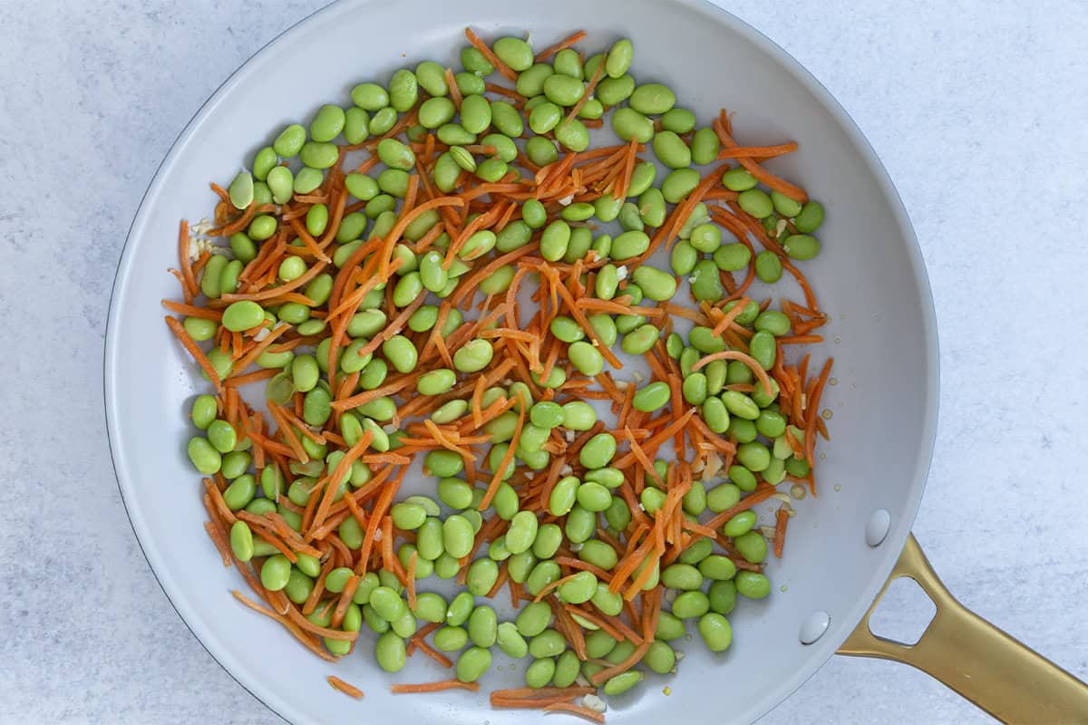 Edamame and carrots cooking in a skillet.
