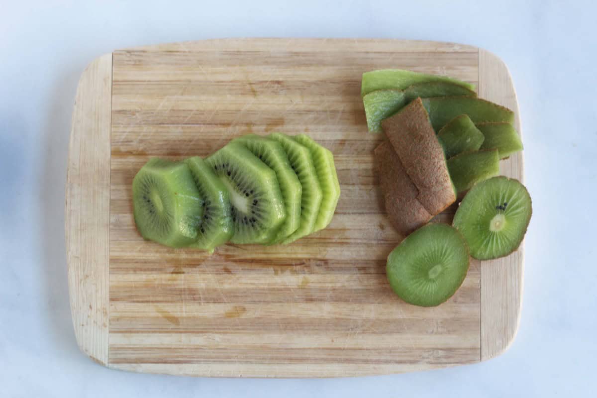 Sliced kiwi and peel on a cutting board.